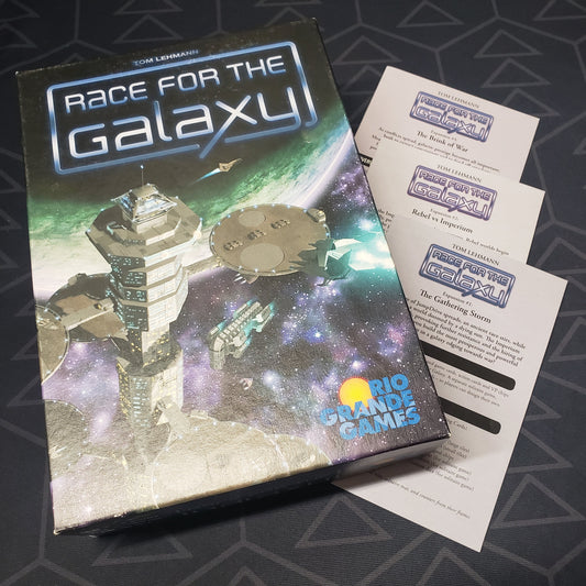 Image shows the front cover of the box for the Race for the Galaxy board game sitting top top of 3 expansion instruction booklets