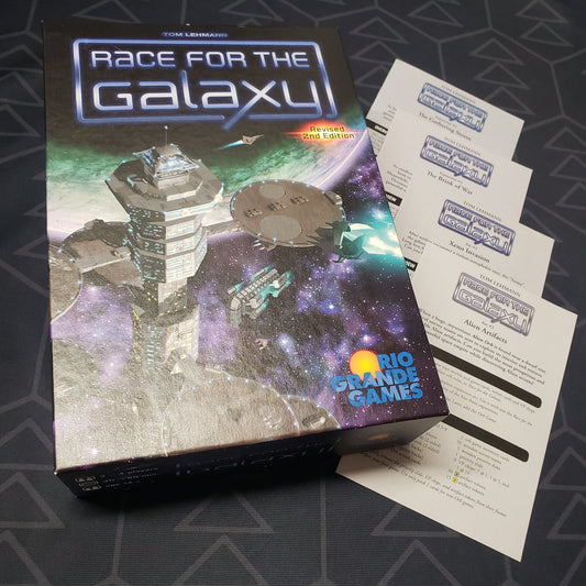 Image shows the front cover of the box for the Race for the Galaxy (Revised Second Edition) board game, with four additional sets of expansion instructions sitting next to it