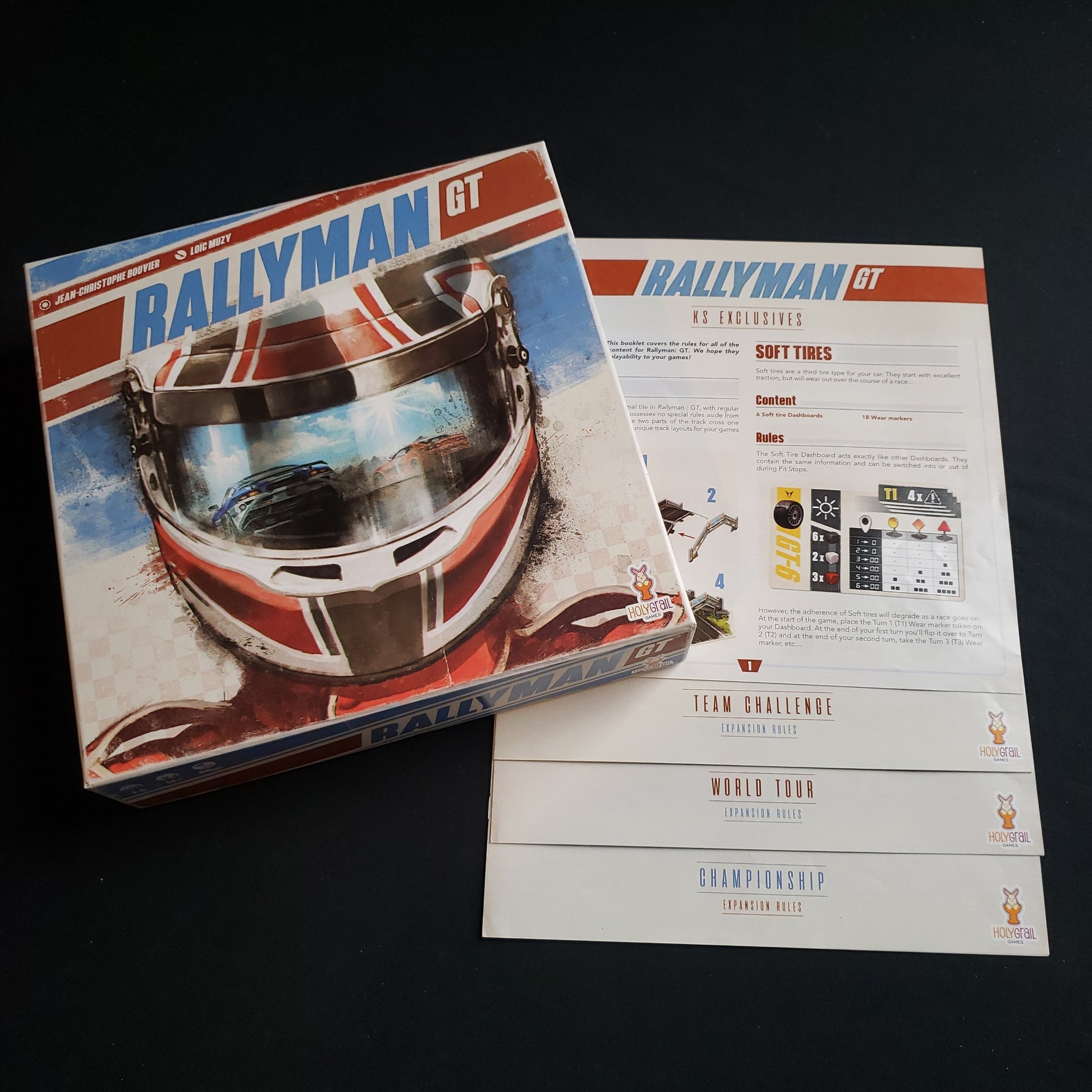 Image shows the front cover of the box of the Rallyman GT board game, sitting on top of instructions for multiple expansions