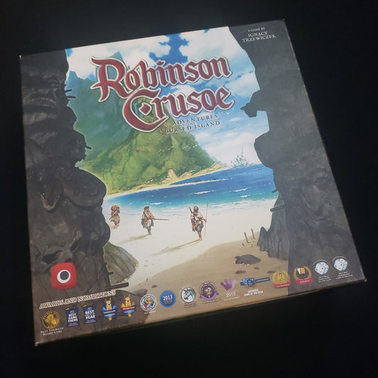 Image shows the front cover of the box of the Robinson Crusoe: Adventures on the Cursed Island board game