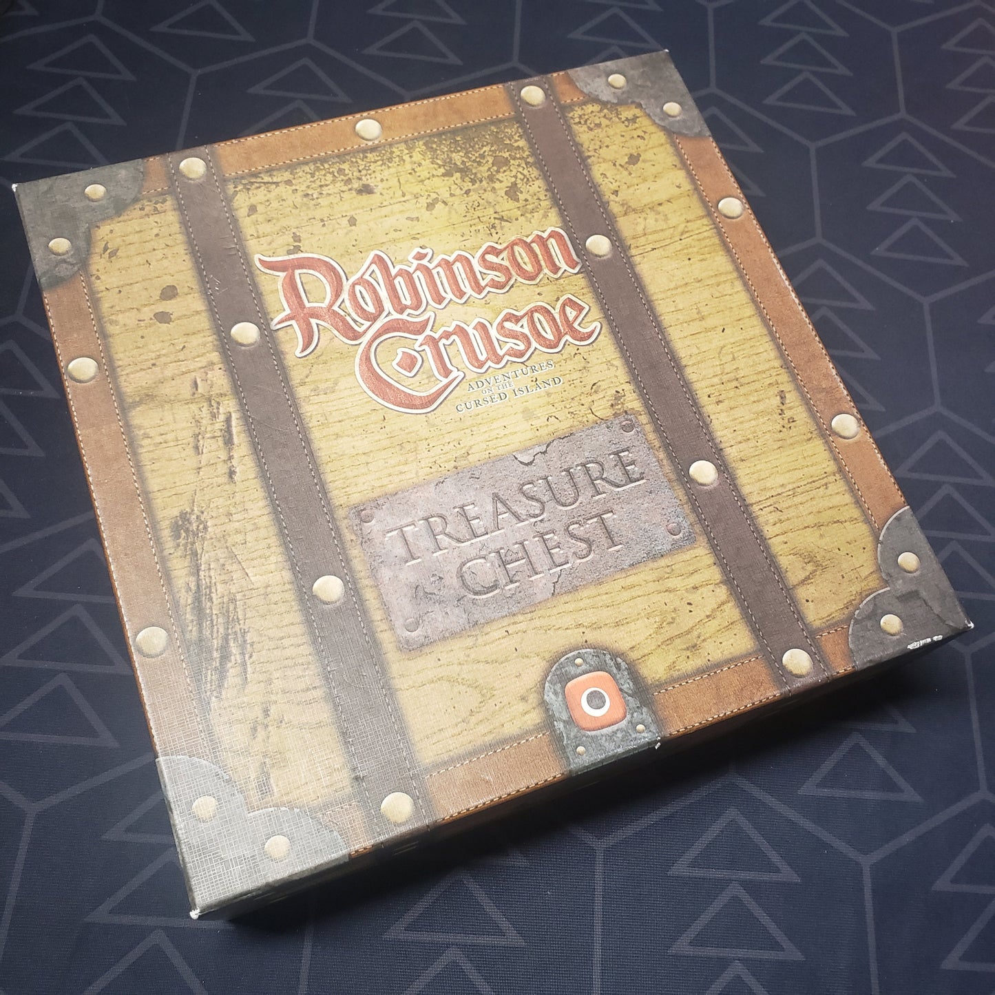 Image shows the front cover of the box of the Treasure Chest expansion for the board game Robinson Crusoe