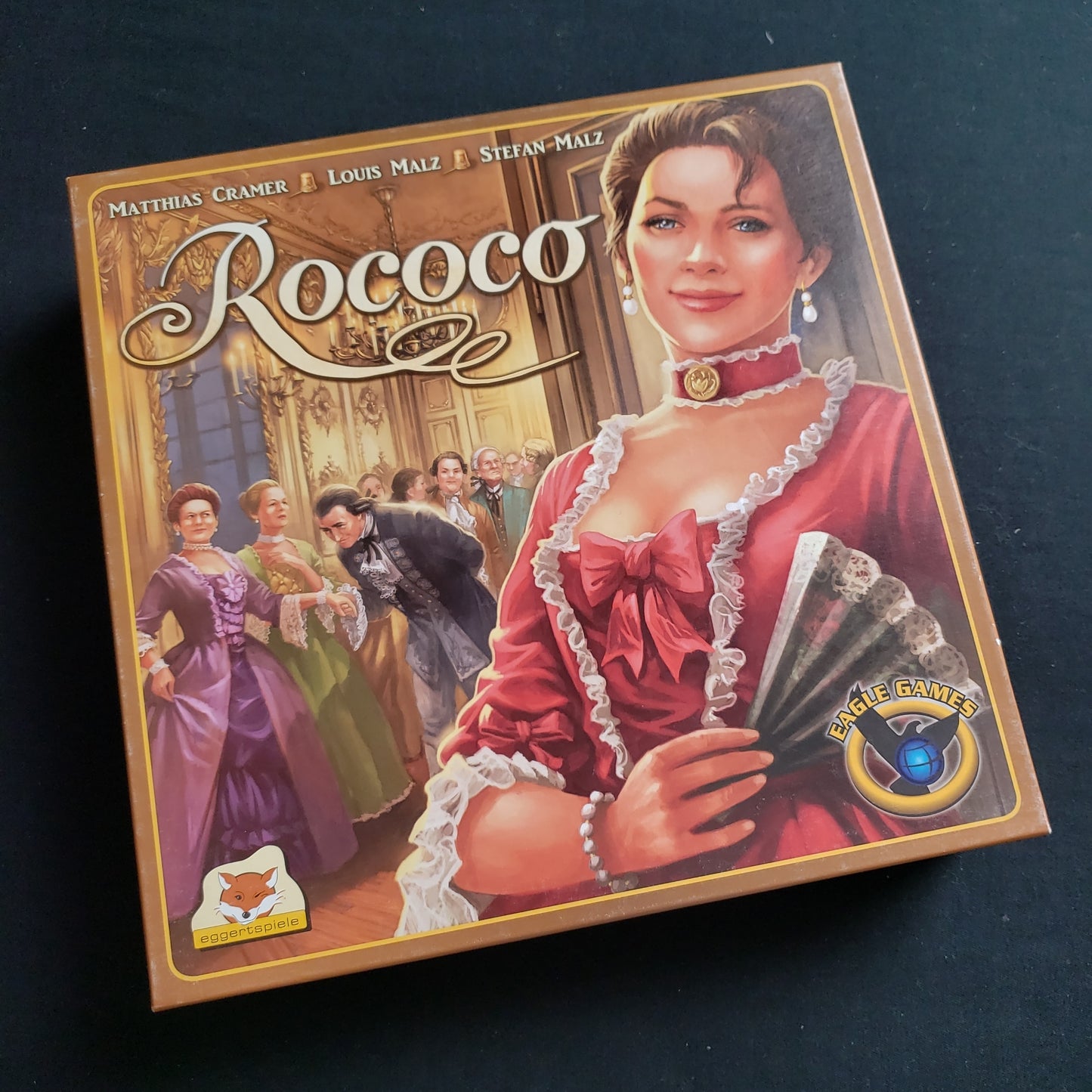 Image shows the front cover of the box of the Rococo board game