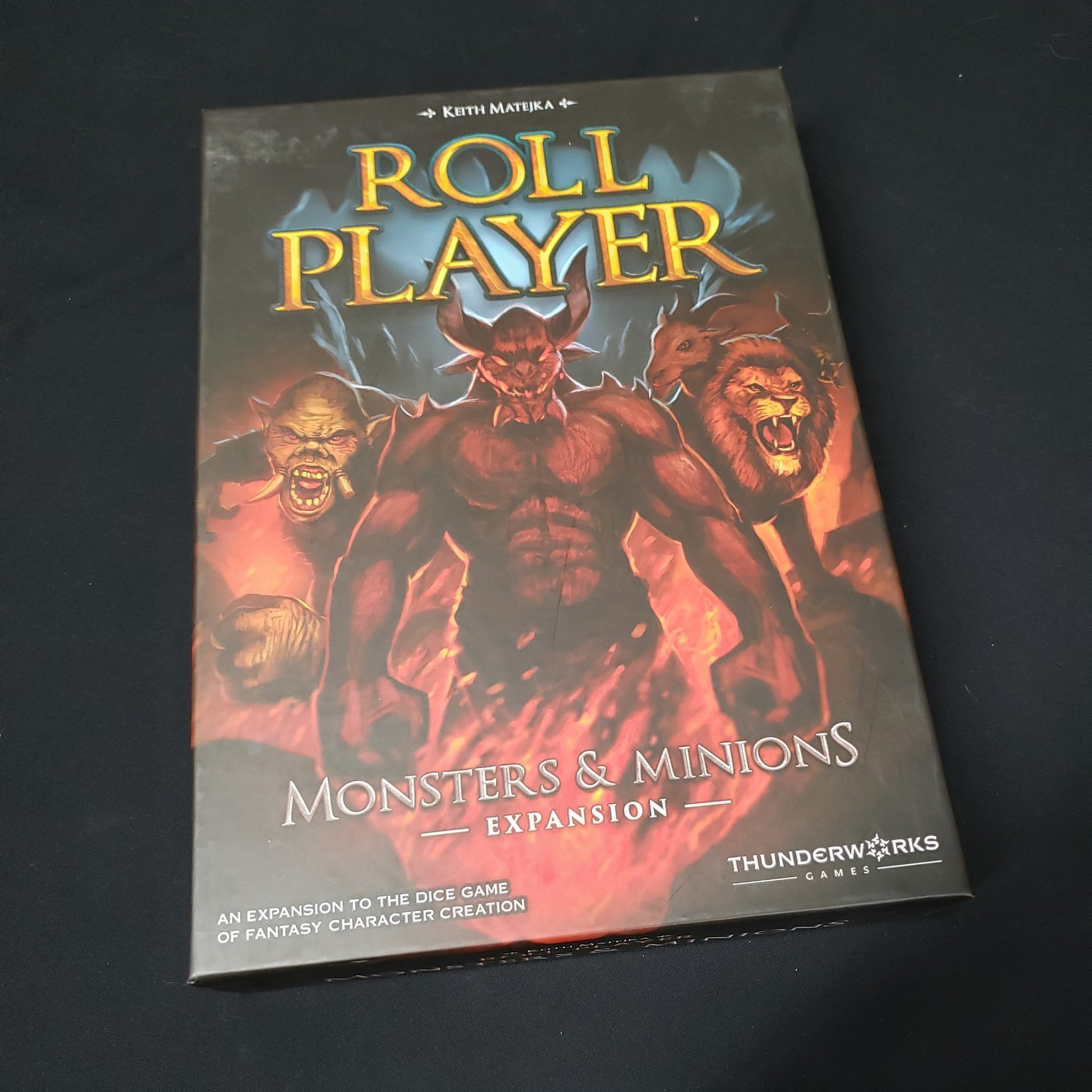 Image shows the front cover of the box of the Monsters & Minions expansion for the board game Roll Player
