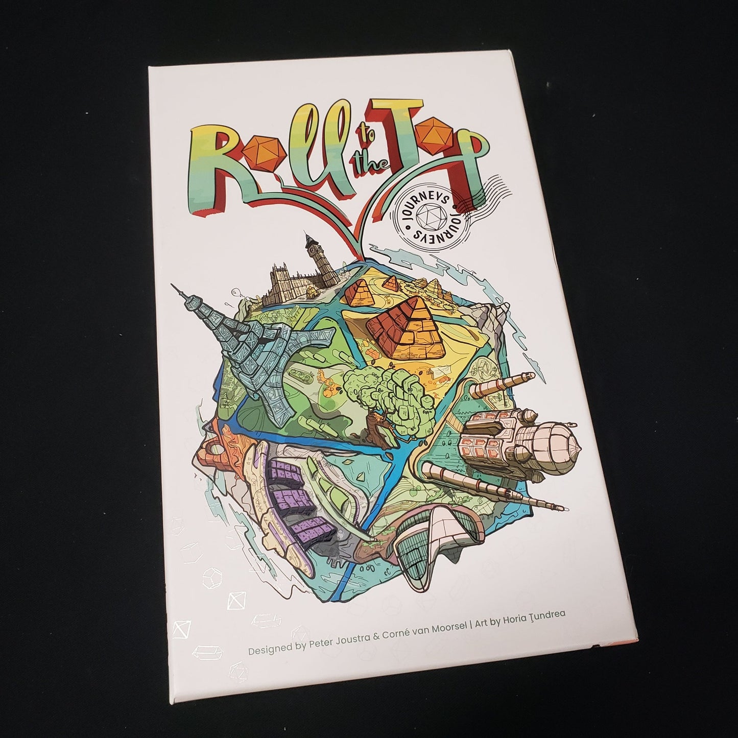 Image shows the front cover of the box of the Roll to the Top: Journeys board game