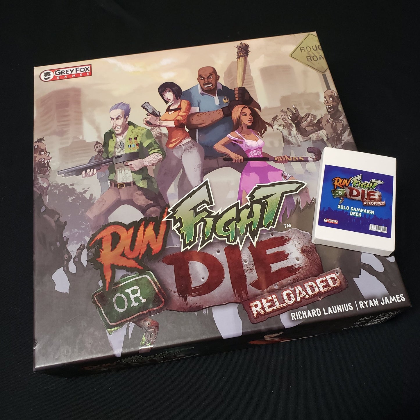 Image shows the front cover of the box of the Run Fight or Die: Reloaded board game with the box for the Solo Campaign Deck sitting on top of it
