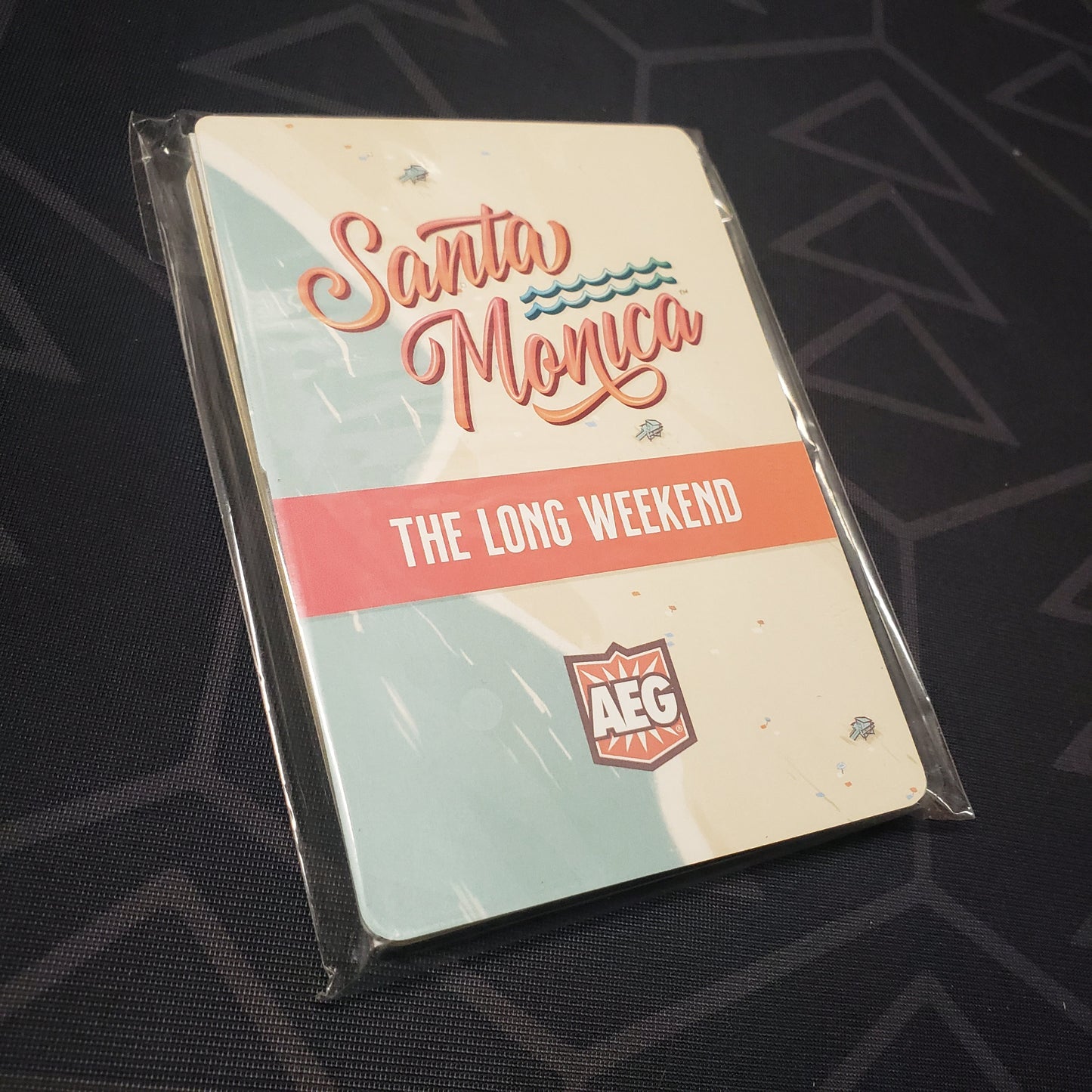 Image shows the front of the packaging for the Long Weekend expansion for the board game Santa Monica