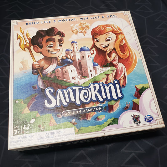 Image shows the front cover of the box of the Santorini board game