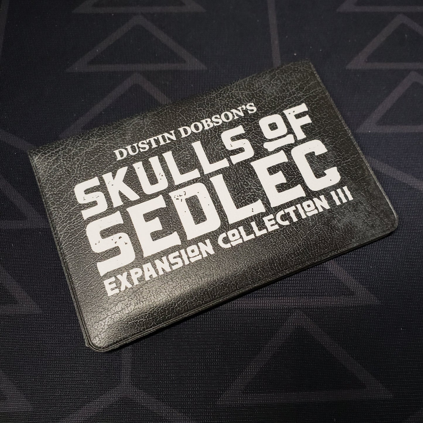 Image shows the front cover of the card wallet of Expansion Collection III for the card game Skulls of Sedlec