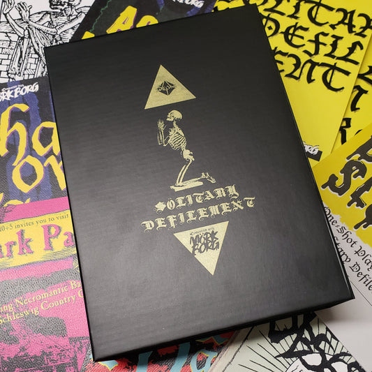 Image shows the front of the limited edition Futility of Prayer box for the roleplaying game Solitary Defilement, with the various zines surrounding it that make up the box set