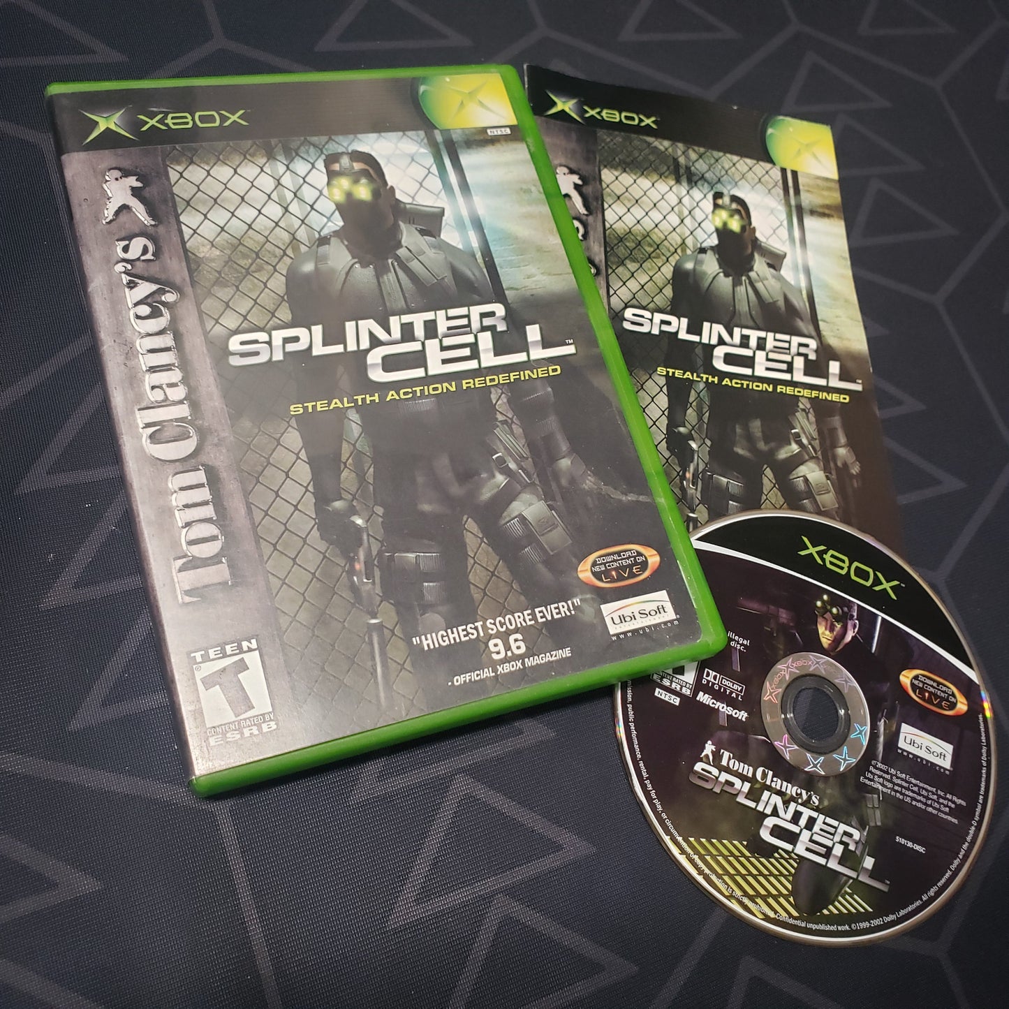 Image shows the case, manual and disc for the video game Splinter Cell for the original Xbox