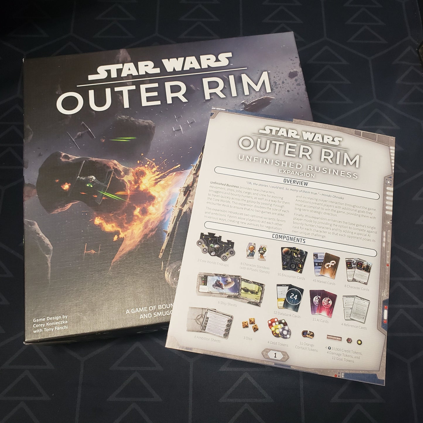 Image shows the front cover of the box of the Star Wars: Outer Rim board game with the instructions for the Unfinished Business expansion sitting on top of it