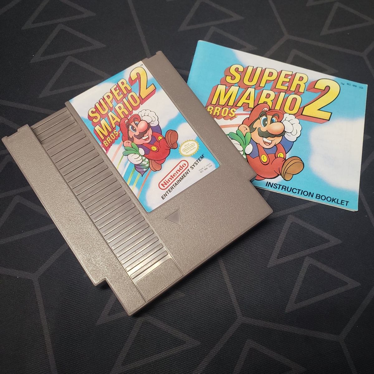 Image shows the front of the cartridge for the video game Super Mario Bros. 2 for the Nintendo Entertainment System and the manual for the game