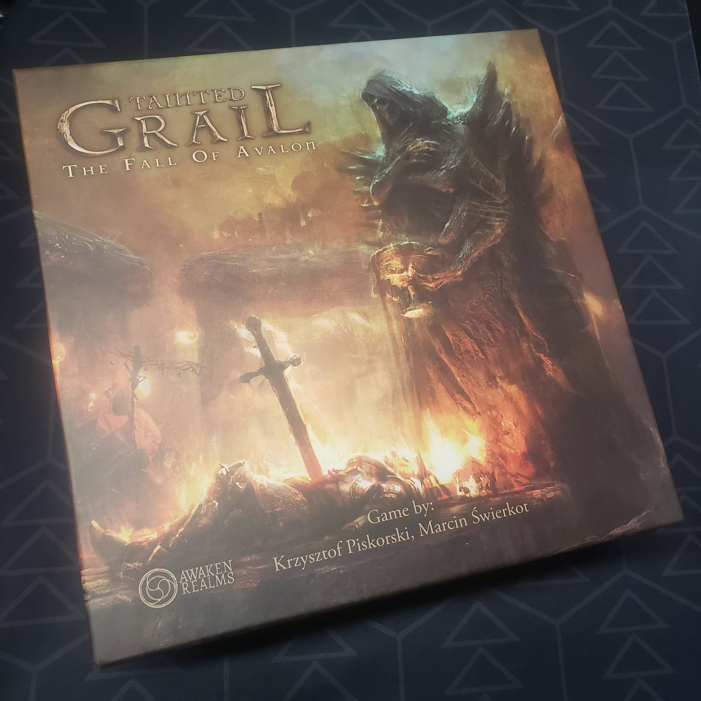 Image shows the front cover of the box of the Tainted Grail board game