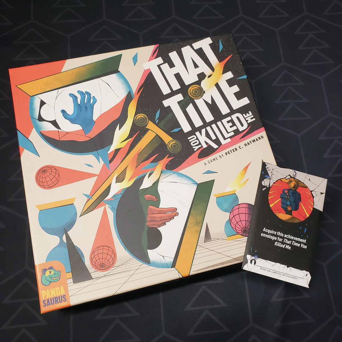 Image shows the front cover of the box of the That Time You Killed Me board game with a promo pack sitting on top of it
