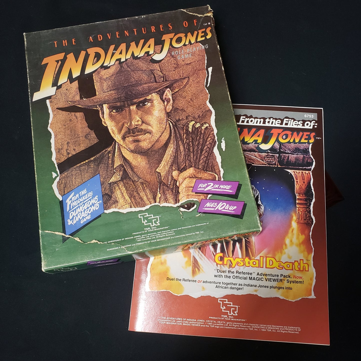 Image shows the front cover of the box of the Adventures of Indiana Jones roleplaying game box set, sitting on top of the Crystal death module