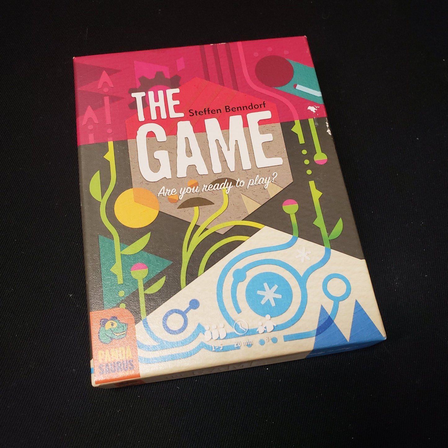 Image shows the front cover of the box of the card game titled The Game