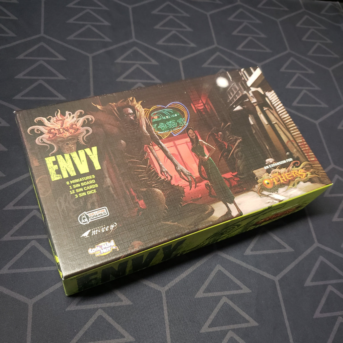 Image shows the front cover of the box of the Envy expansion for the board game The Others