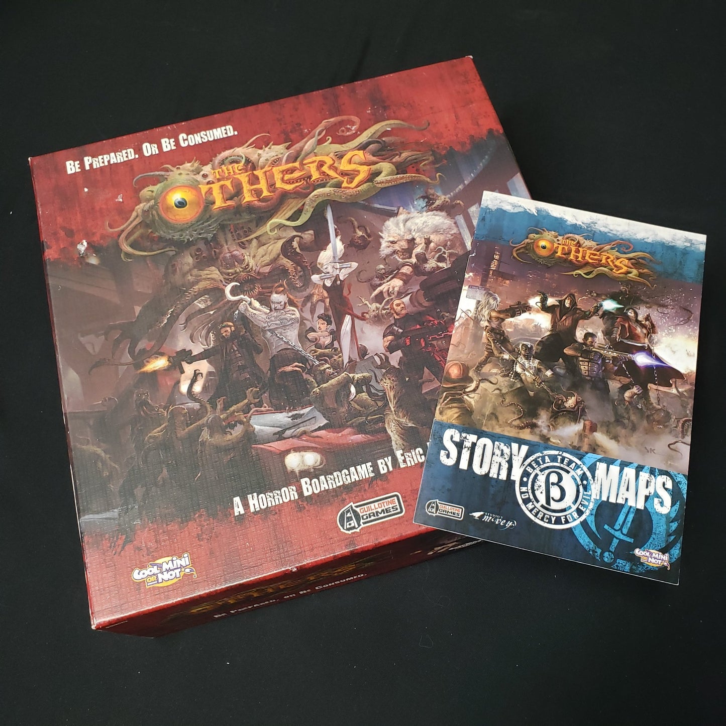Image shows the front cover of the box of the Others board game, with the instructions for the Beta Team expansion sitting on top of it