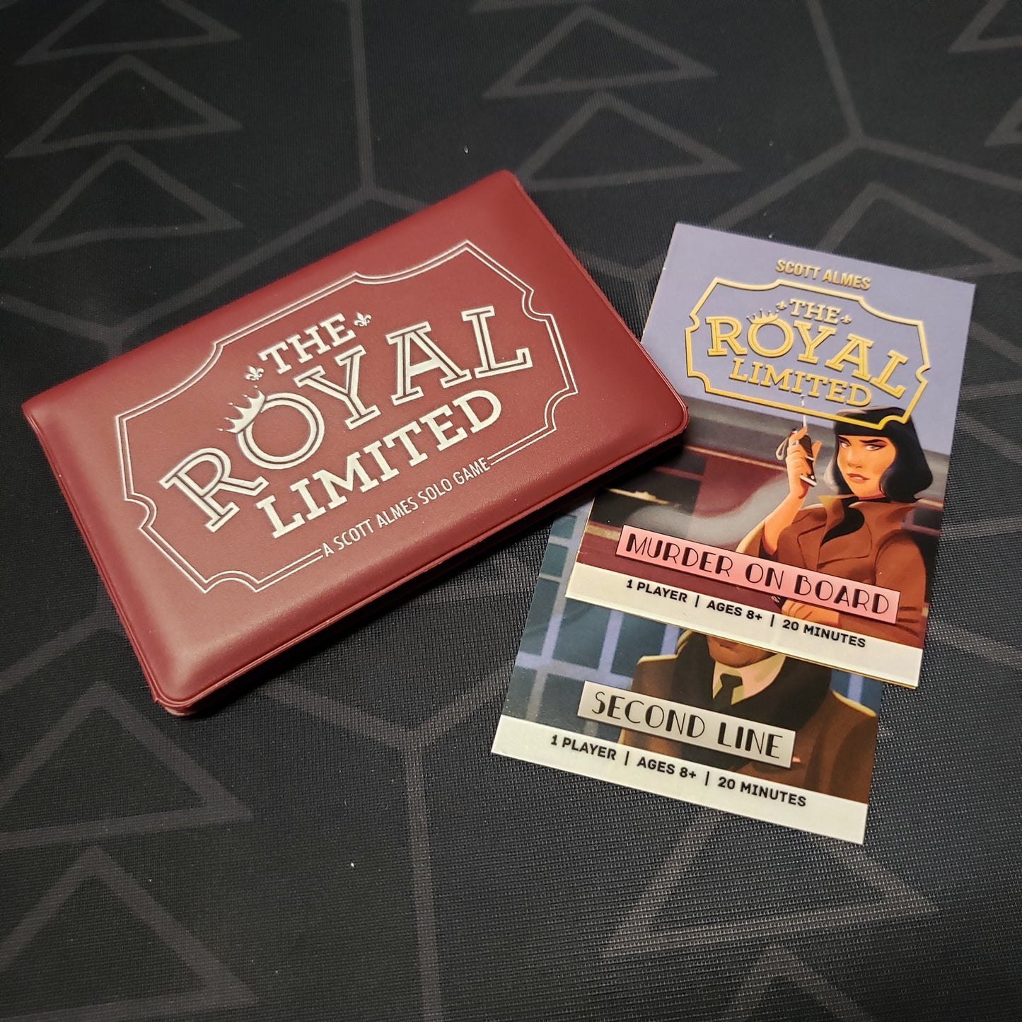 Image shows the front of the card wallet for the card game The Royal Limited, with the Murder on Board & Second Line expansions sitting next to it