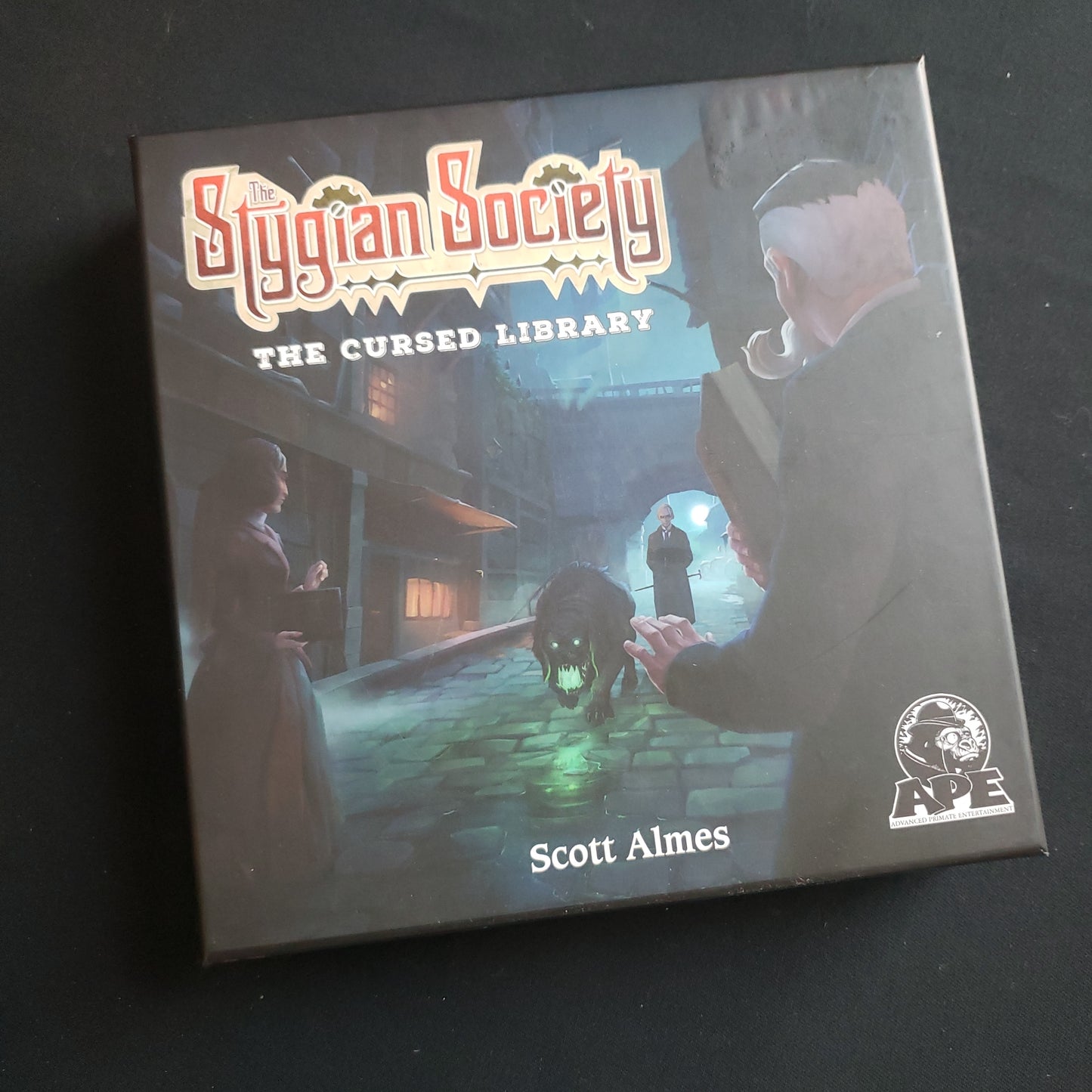 Image shows the front cover of the box of the Cursed Library expanison for the board game The Stygian Society