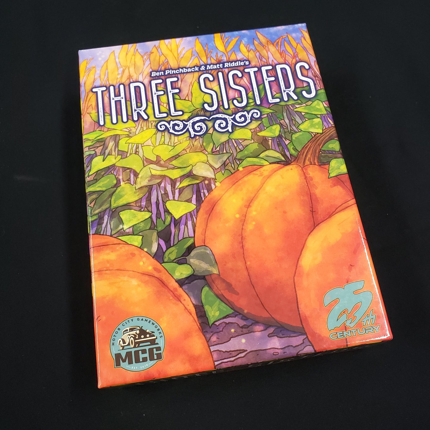 Image shows the front cover of the box of the Three Sisters board game