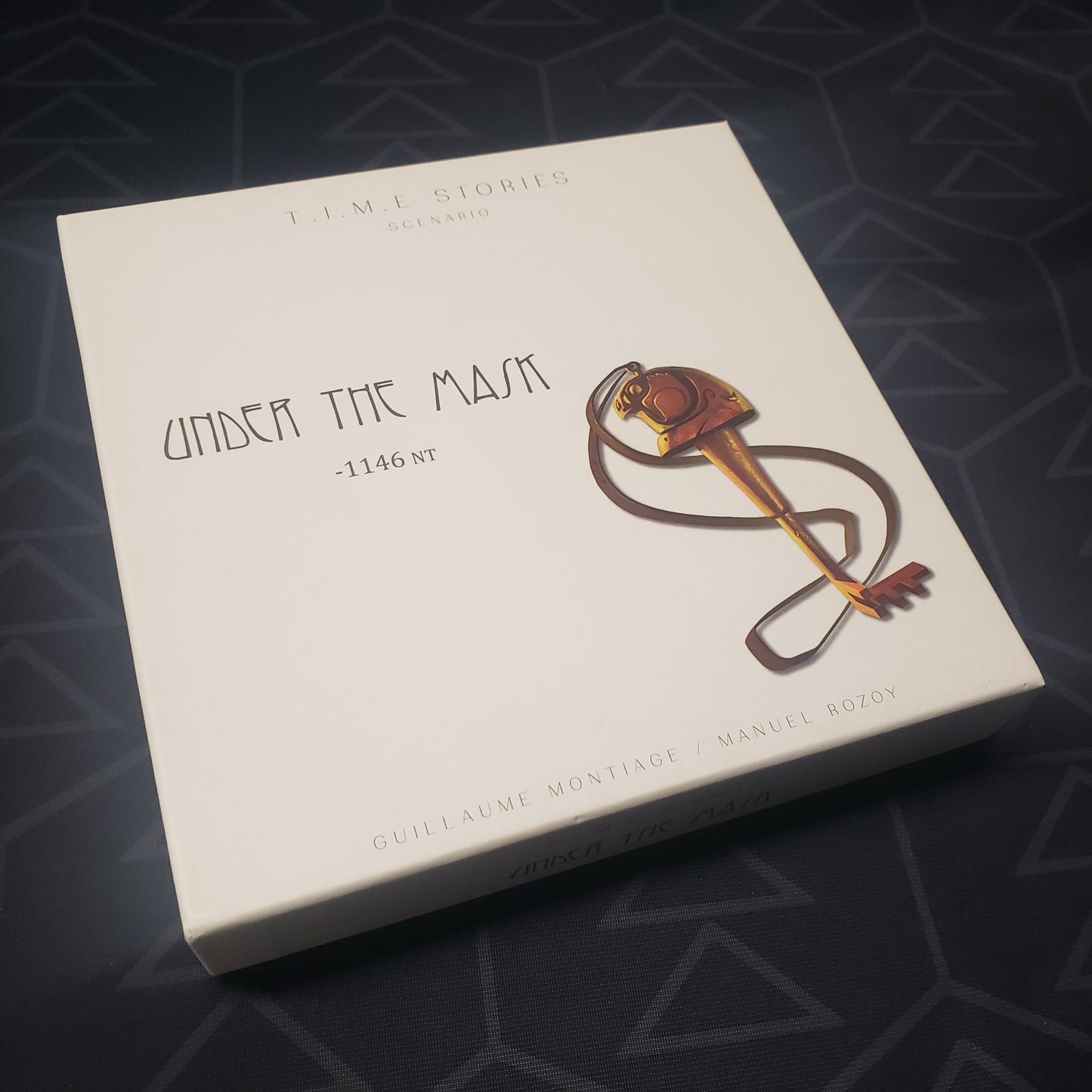 Image shows the front cover of the box of the Under the Mask expansion for the board game TIME Stories