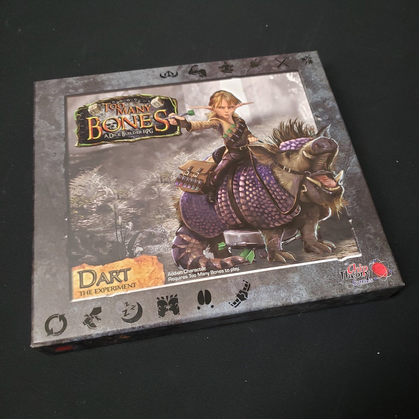 Image shows the front cover of the box for the Dart expansion from the board game Too Many Bones