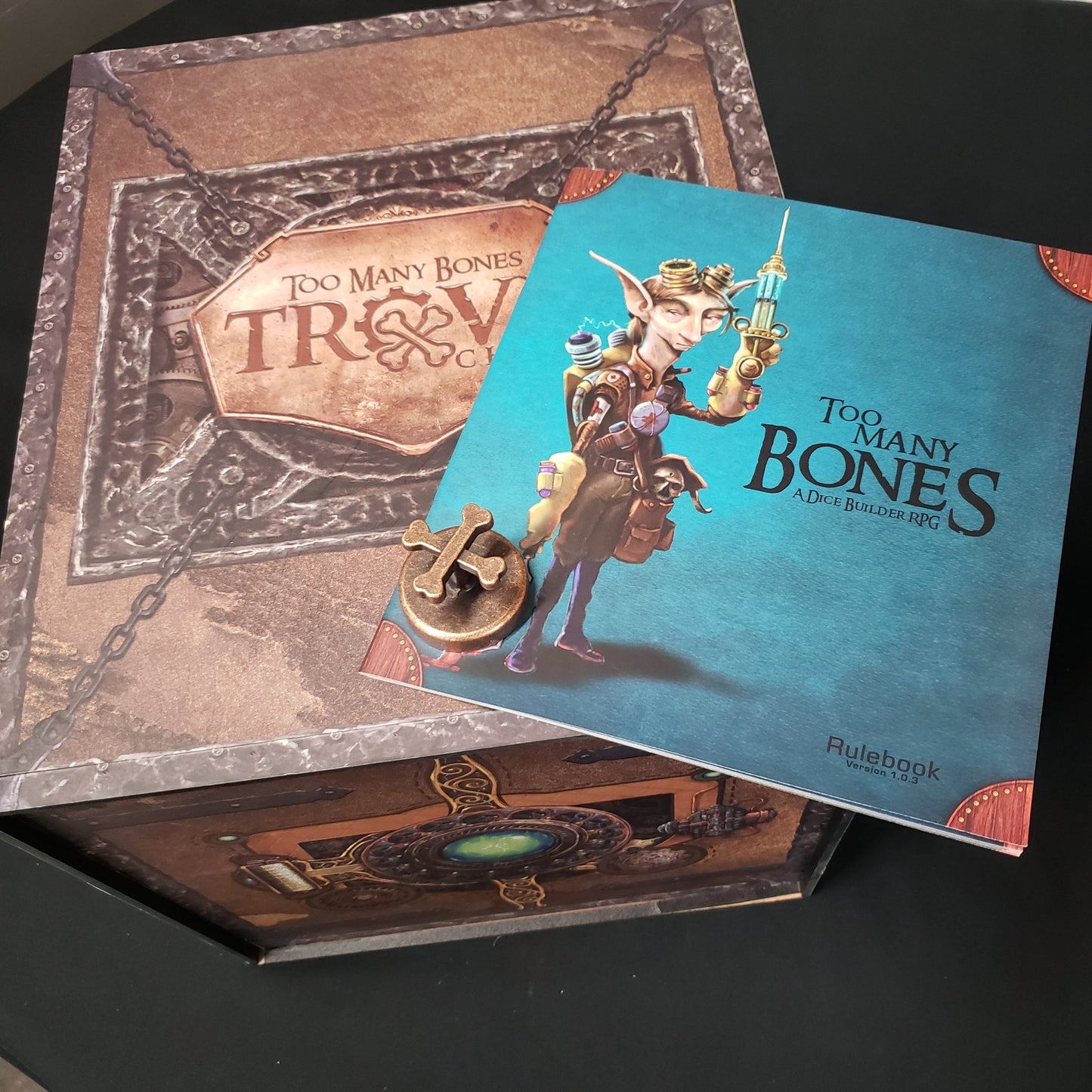 Image shows the rules booklet from the board game Too Many Bones sitting on tope of the Trove Chest deluxe storage solution