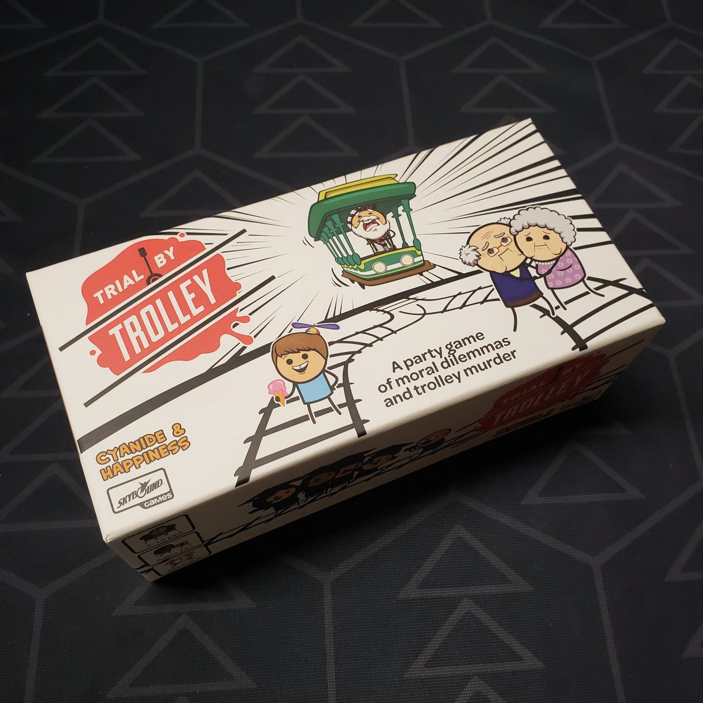 Image shows the front cover of the box for the Trial by Trolley card game
