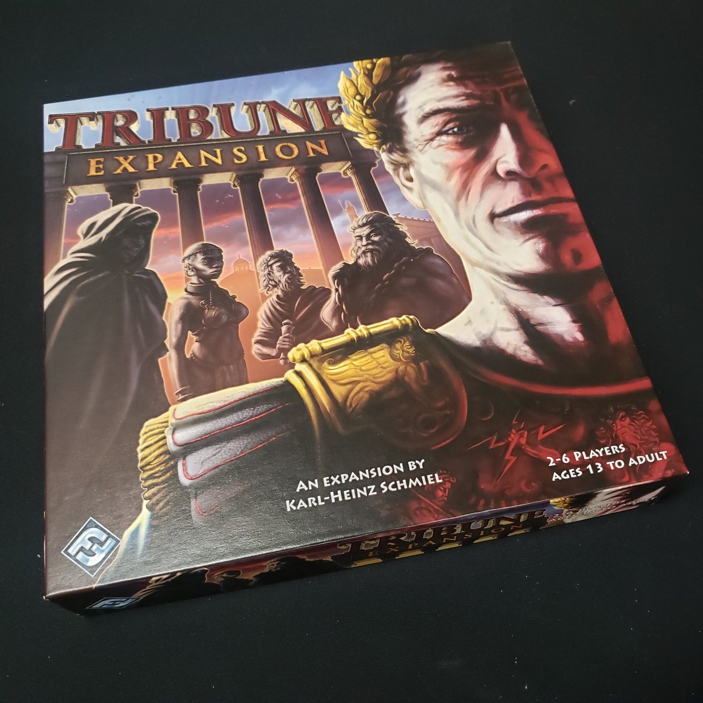 Image shows the front cover of the box of the expansion for the board game Tribune