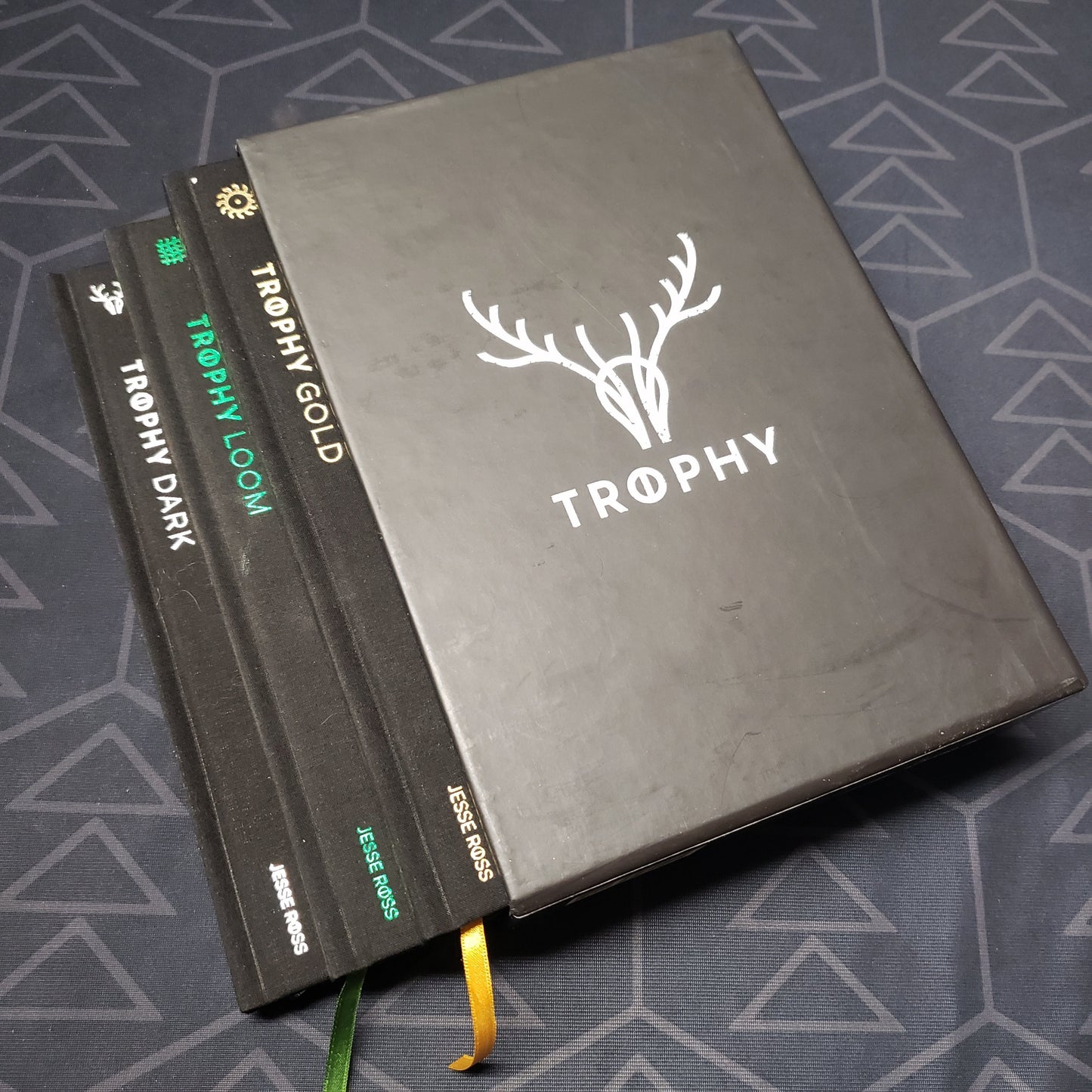 Image shows the front of the box for the Trophy: Hardcover Collection roleplaying game set, with the Dark, Gold & Loom books fanned out from the box