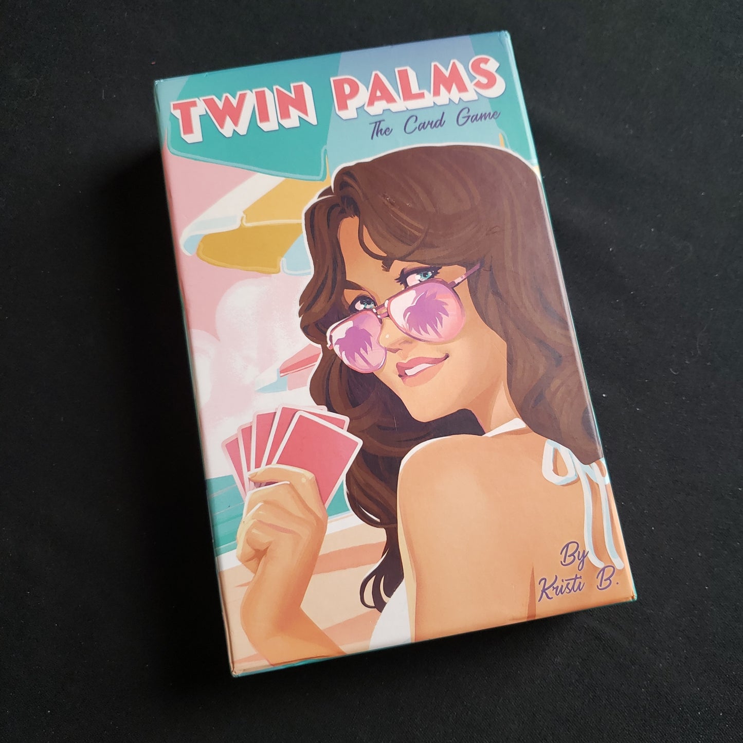 Image shows the front cover of the box of the Twin Palms card game