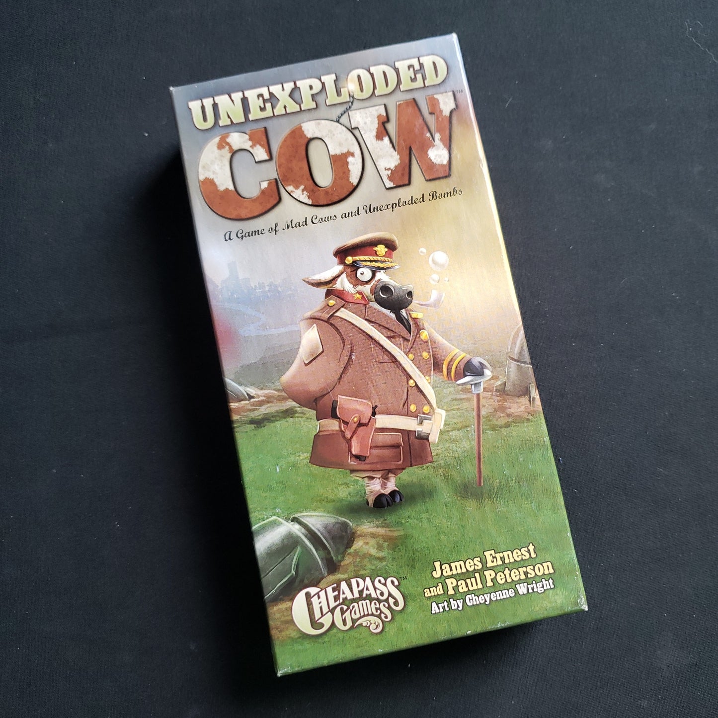 Image shows the front cover of the box of the Unexploded Cow card game
