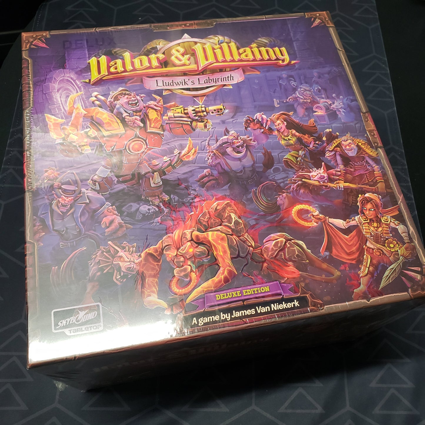 Image shows the front cover of the Deluxe Edition box for the board game Valor & Villainy: Lludwik's Labyrinth