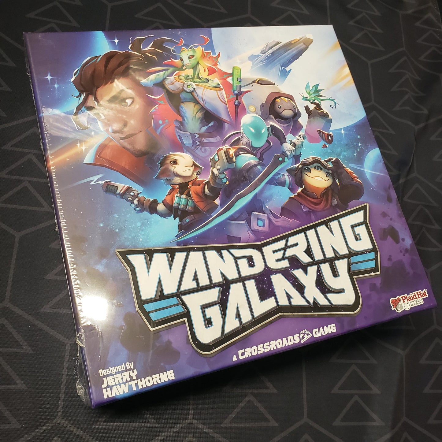 Image shows the front cover of the box for the board game Wandering Galaxy: A Crossroads Game