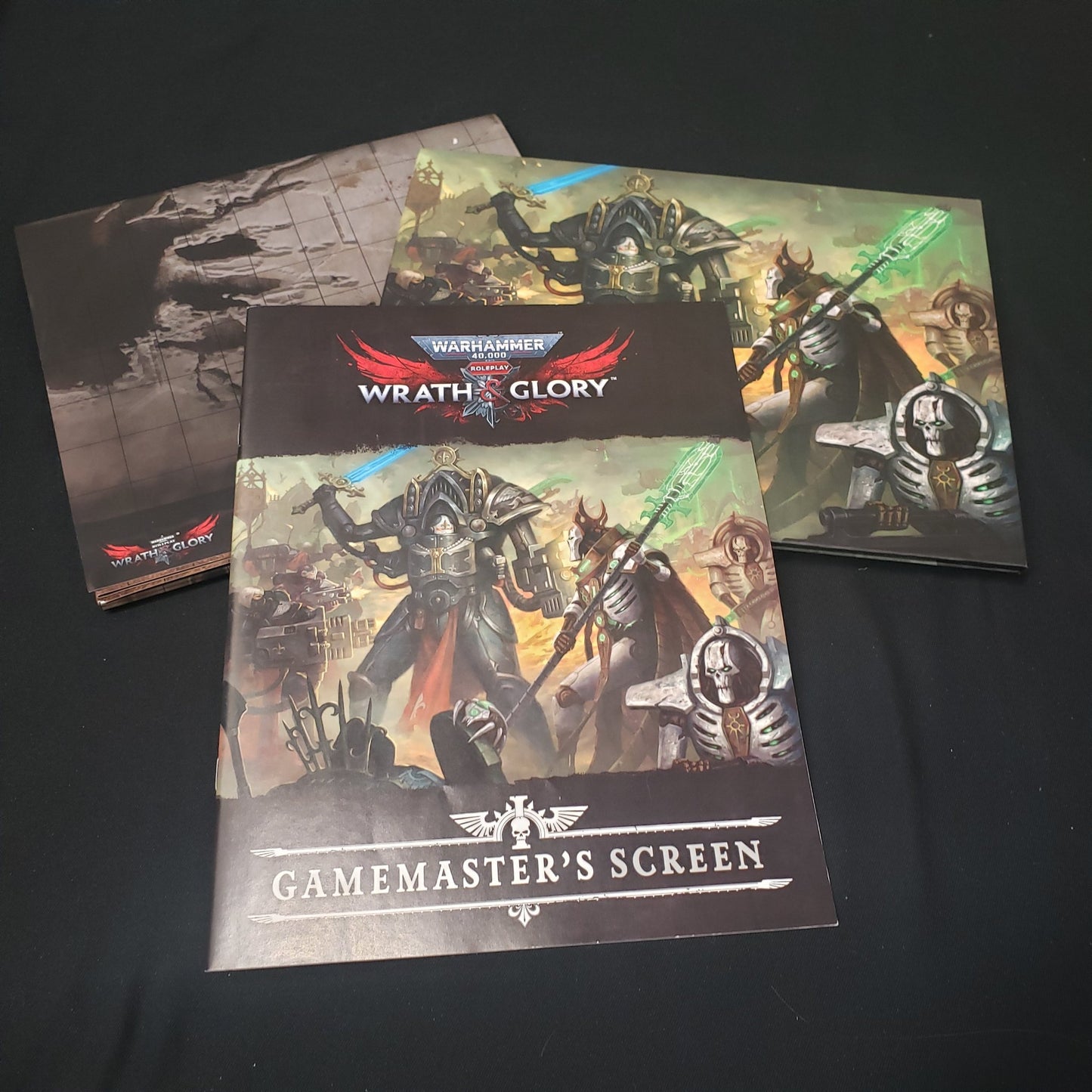 Image shows a scenario book, battlemat, and gamemaster screen for the roleplaying game Wrath & Glory