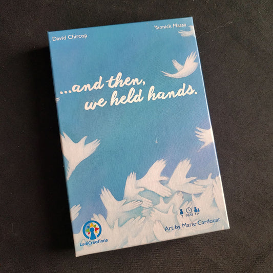 Image shows the front cover of the box of the And Then We Held Hands card game