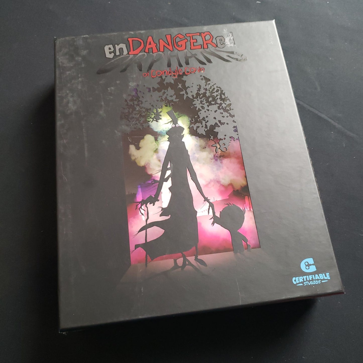 Image shows the front cover of the box of the Endangered Orphans of Condyle Cove board game