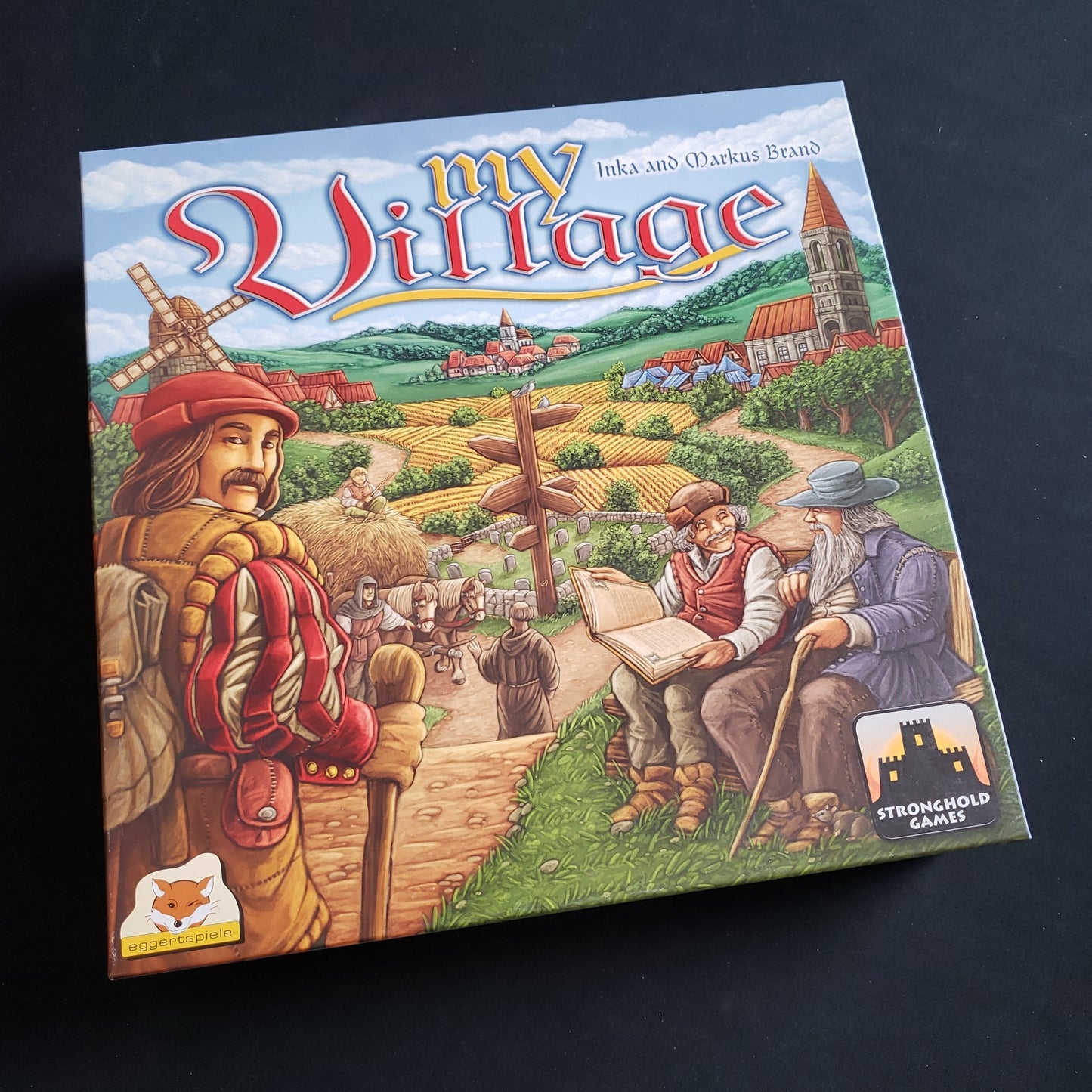 Image shows the front cover of the box of the My Village board game
