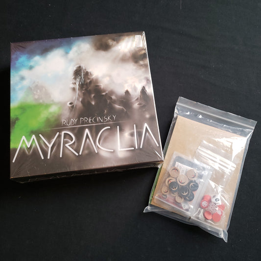 Image shows the front cover of the box of the Myraclia board game, along with the Luna expansion in a clear plastic bag next to it