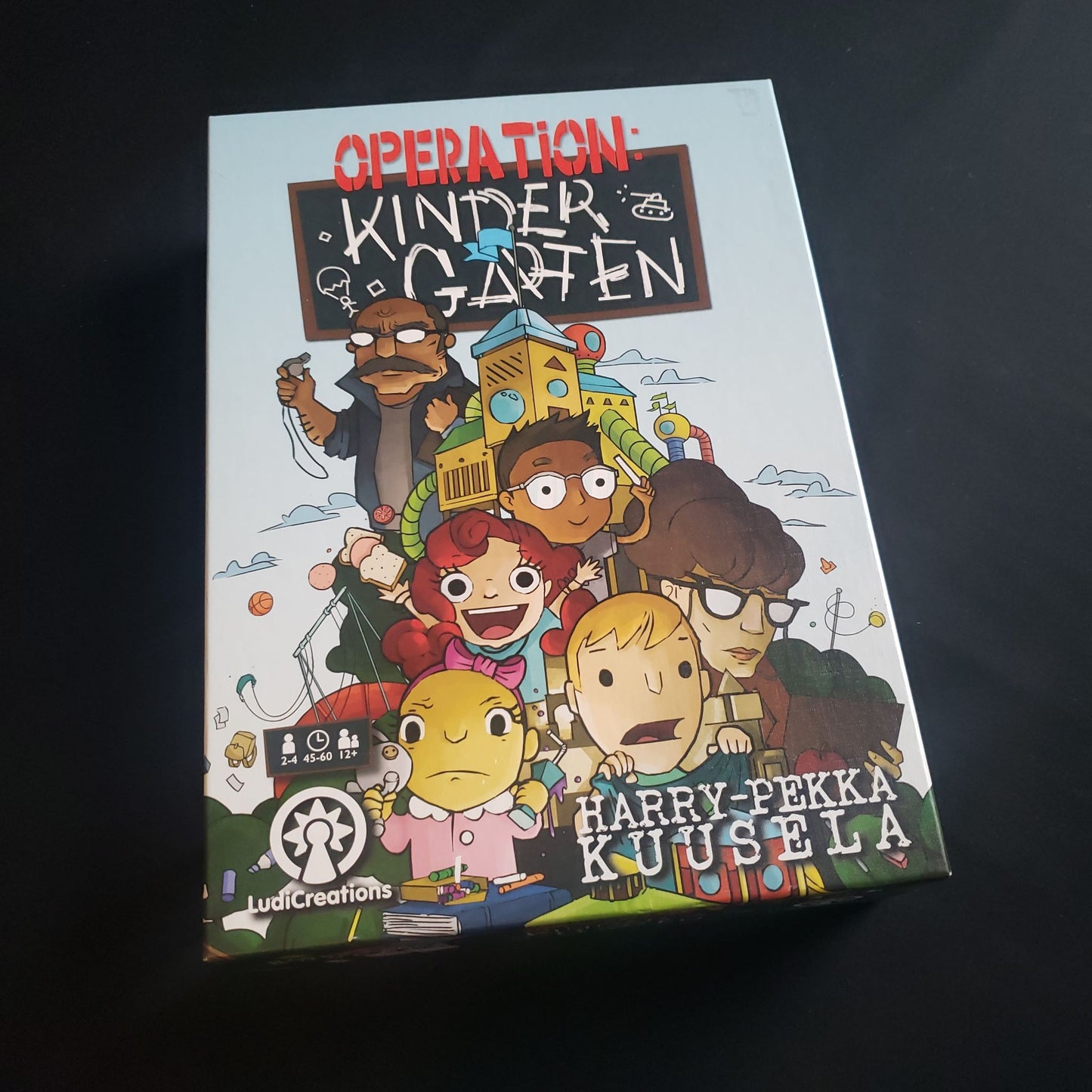 Image shows the front cover of the box of the Operation Kindergarten board game
