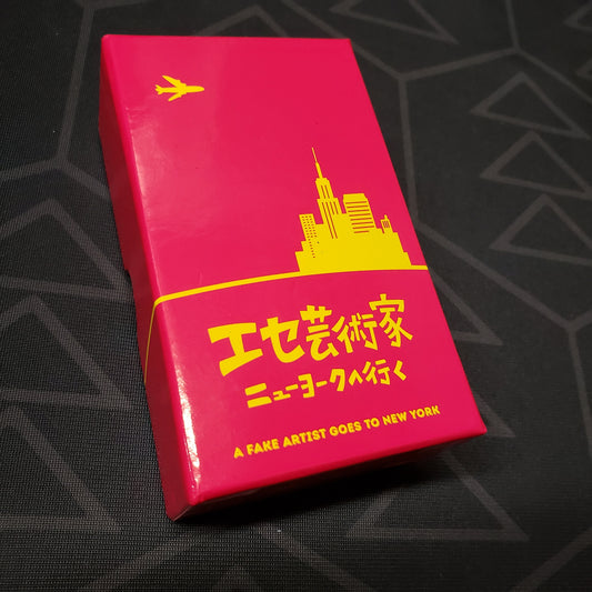 Image shows the front cover of the box of the multilingual edition of the board game A Fake Artist Goes to New York