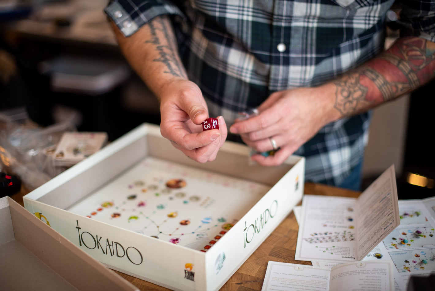 Image shows an employee holding a die while counting the pieces in the Tokaido board game. Instruction manuals and components are also laid out on a table.