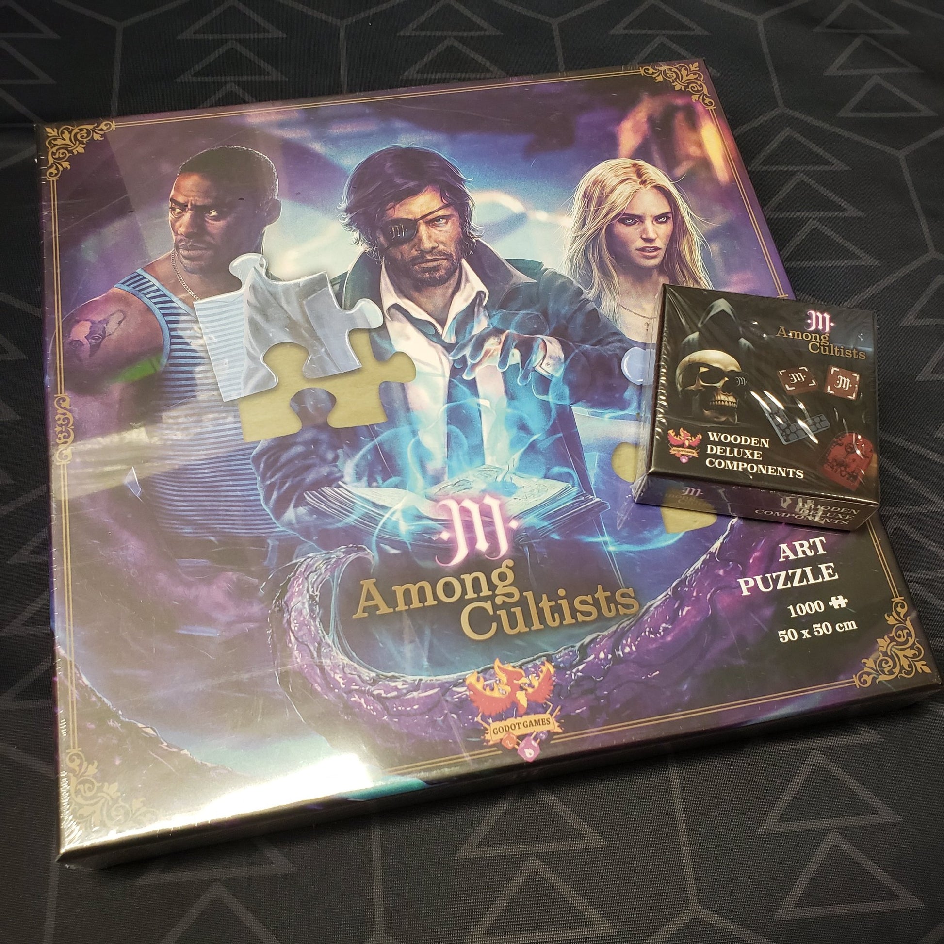 Image shows the front cover of the boxes of the Art Puzzle and Wodden Deluxe Components for the board game Among Cultists