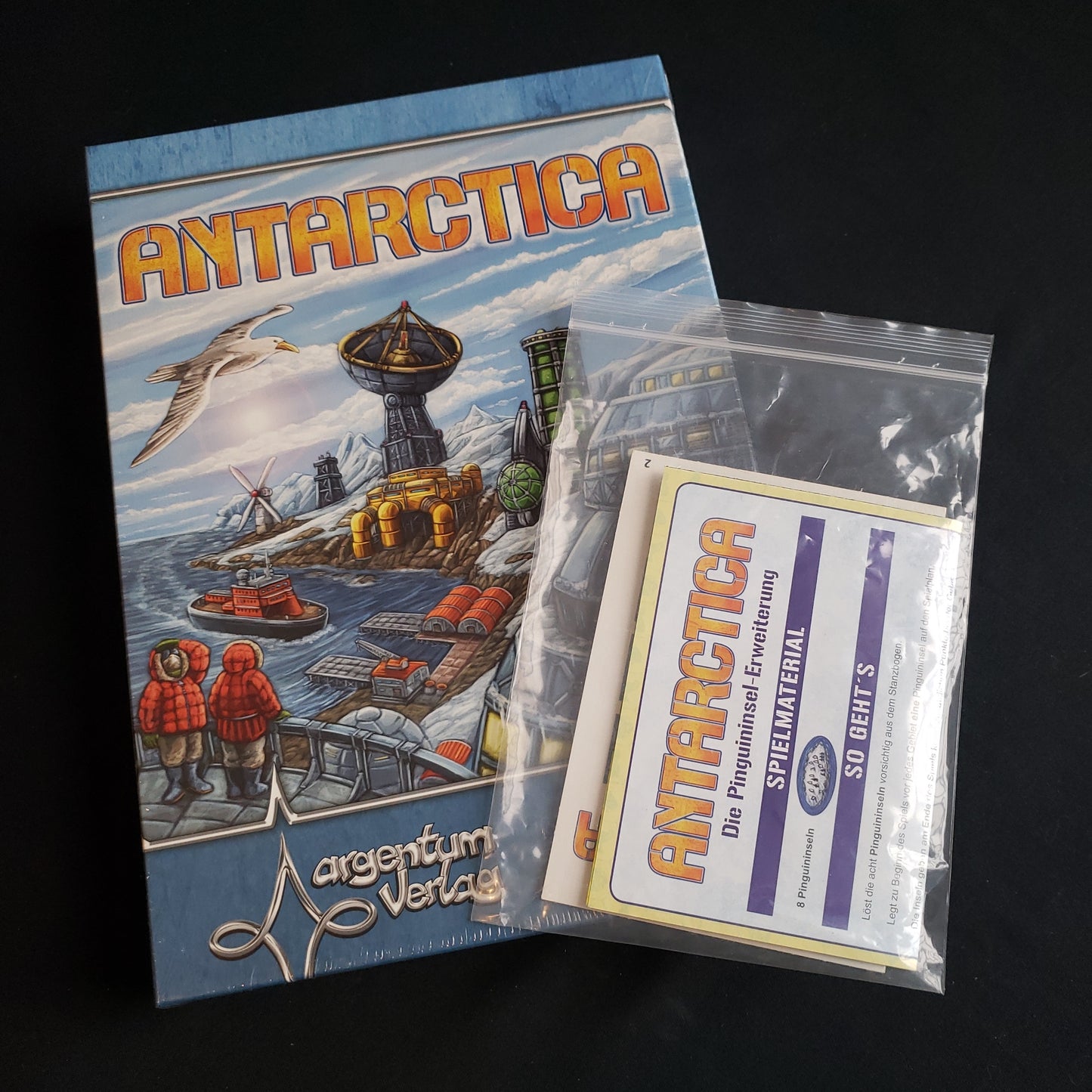 Image shows the front cover of the box of the Antarctica board game, with a bag with the Penguins expansion in it sitting on top