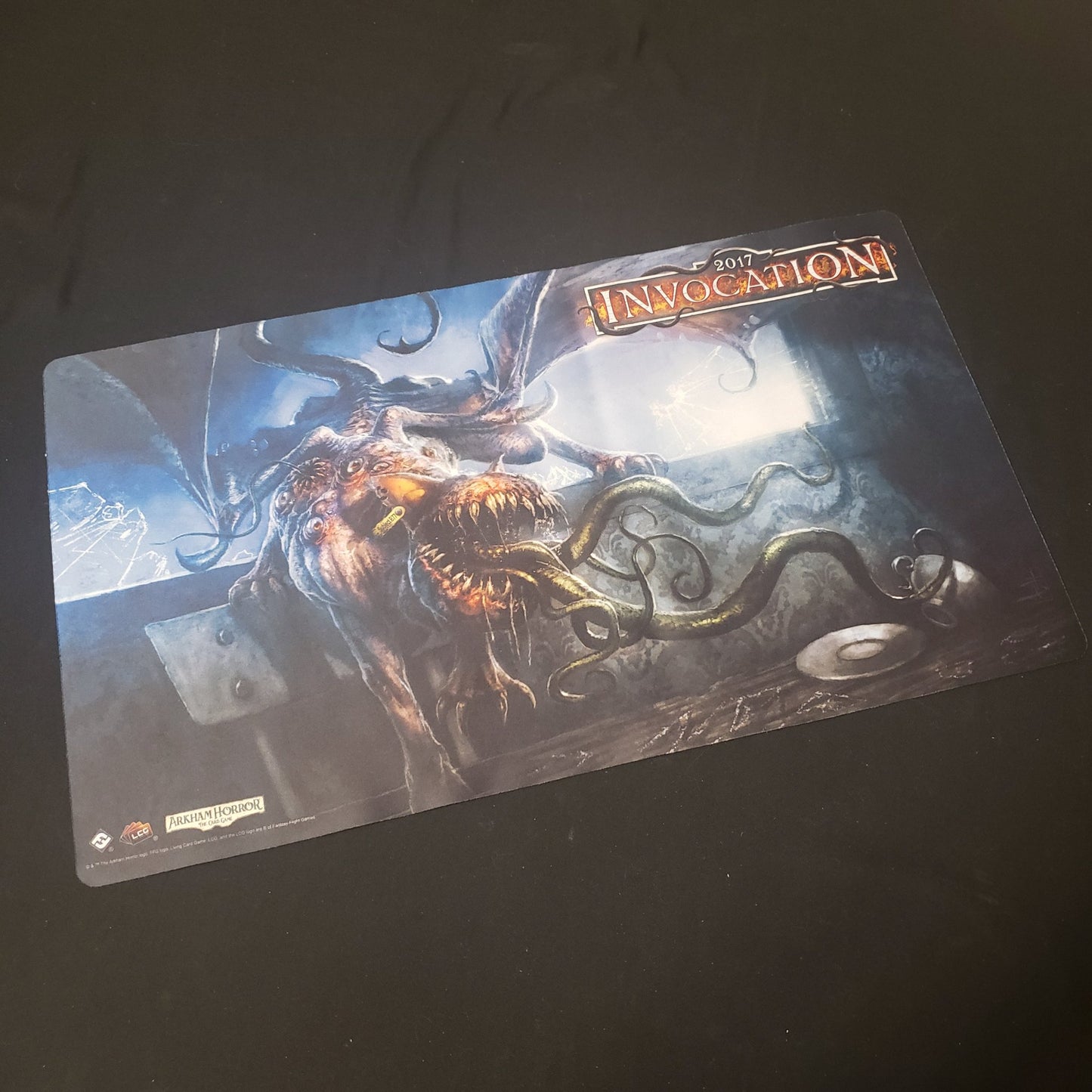 Image shows a promotional playmat from 2017 Invocation events for the Arkham Horror Card Game