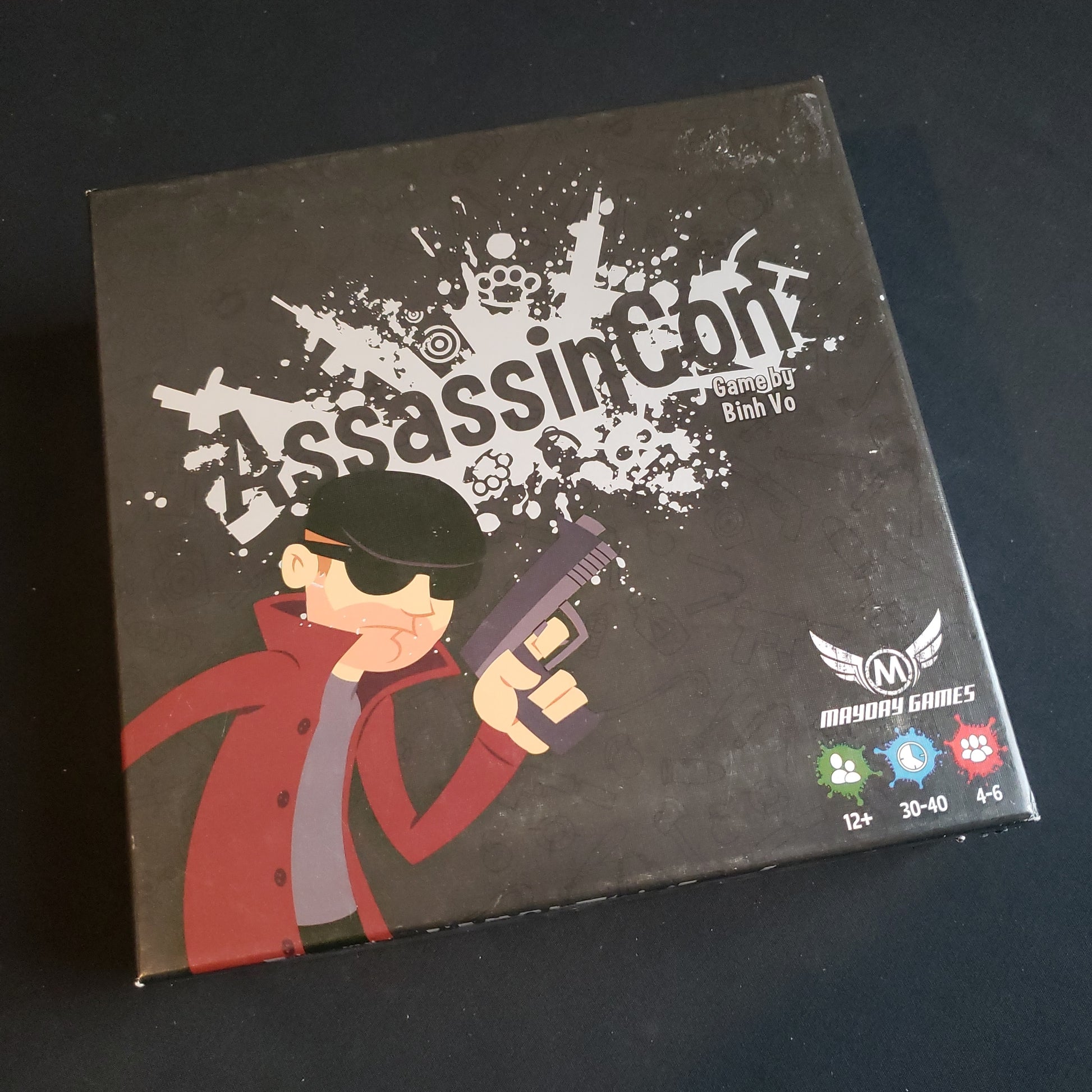 Image shows the front cover of the box of the AssassinCon board game