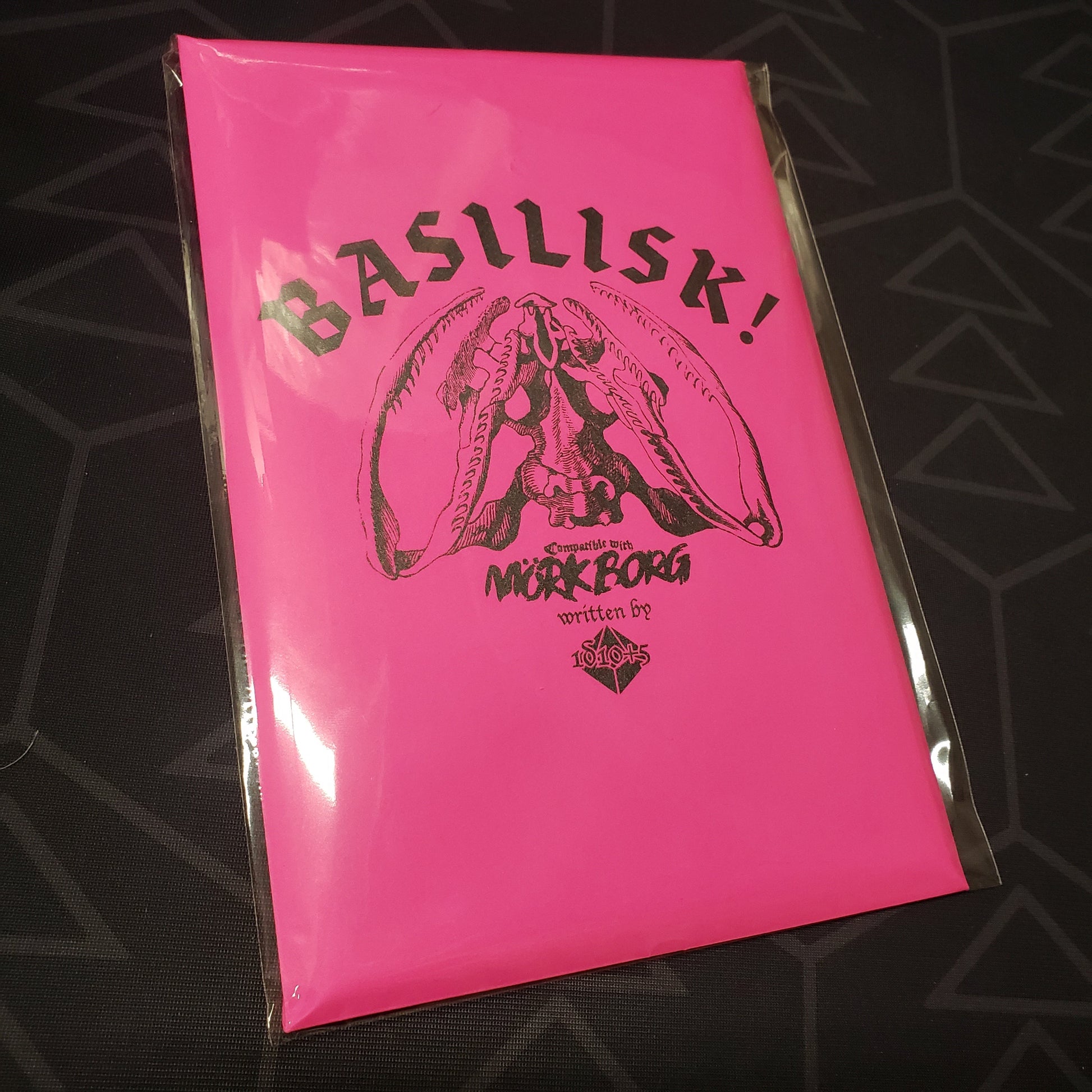 Image shows the front of the package for the hot pink 2025 edition of the roleplaying game BASILISK!