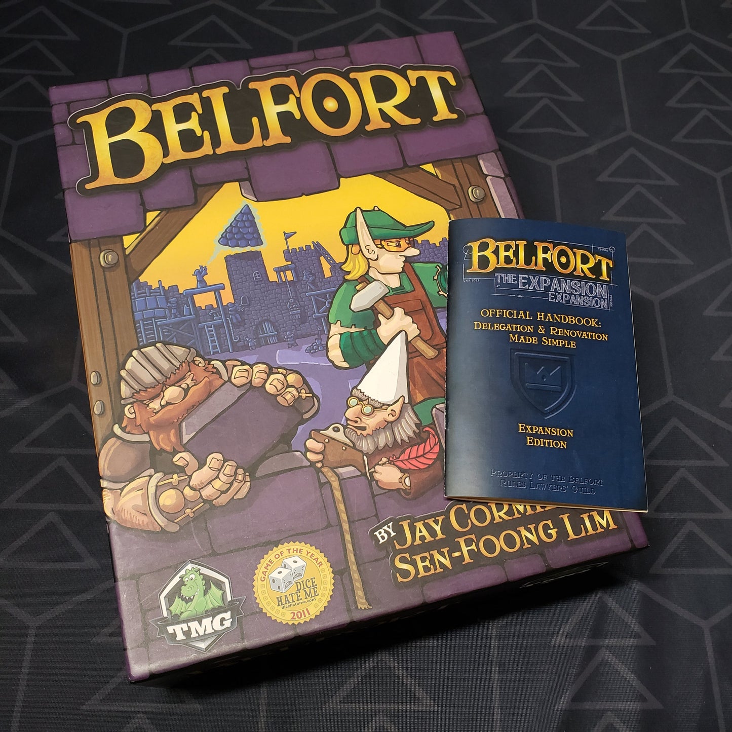 Image shows the front cover of the box of the Belfort board game with the expansion instructions sitting on top of it