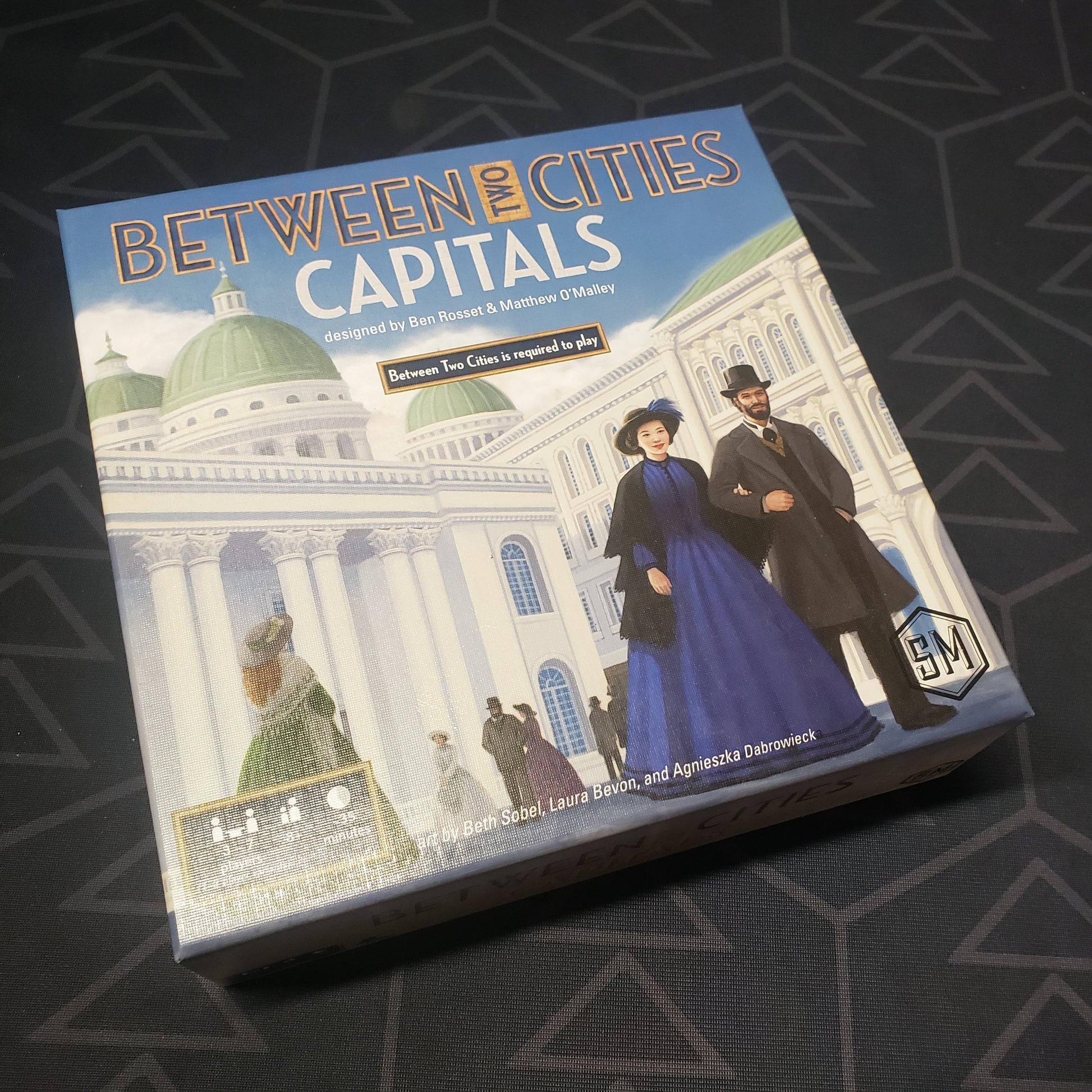 Image shows the front cover of the box of the Capitals expansion for the board game Between Two Cities